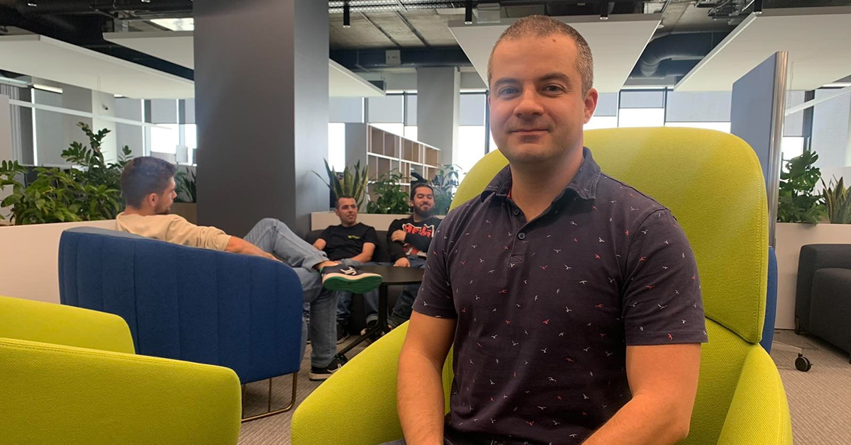 Hristian Kostov seated on a green chair at the Amusnet office commenting on the  company internship 